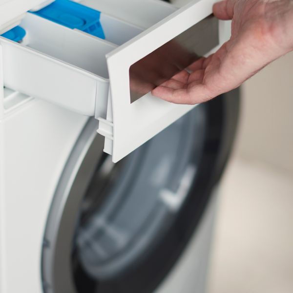 Main retirant le tiroir à lessive d'une machine à laver pour le nettoyer