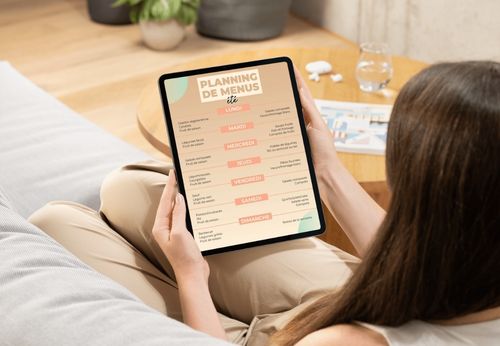 Femme consultant son planning repas d'été sur une tablette, assise sur son canapé
