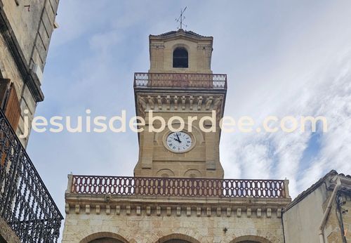 Tour de l'horloge de Vauvert Gard, en pierre, avec son cadran et ses balustrades sous un ciel nuageux